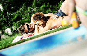 Faulenzen auf der Liegewiese, © weinfranz.at Ein Paar liegt entspannt auf einer Wiese neben einem Pool.