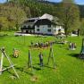 Pension Kobichl, © zVg Kinder spielen auf einem Spielplatz vor einem großen Haus in einer grünen Landschaft.
