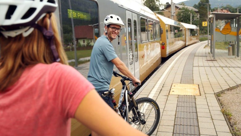 Mariazell Railway "The stairway to heaven", © weinfranz.at Two people with bicycle helmets are pushing their bikes on the platform, next to them the stairway to heaven is standing on the tracks.