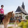 Riding lessons are also offered at the Schaglhof, © Fred Lindmoser Two female riders on horses in front of a building with a tower.