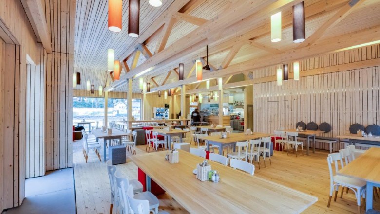 Innenansicht eines modernen Restaurants mit Holzm&ouml;beln und bunten H&auml;ngelampen.