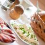 A breakfast table with cheese, ham, bread rolls and herbs.