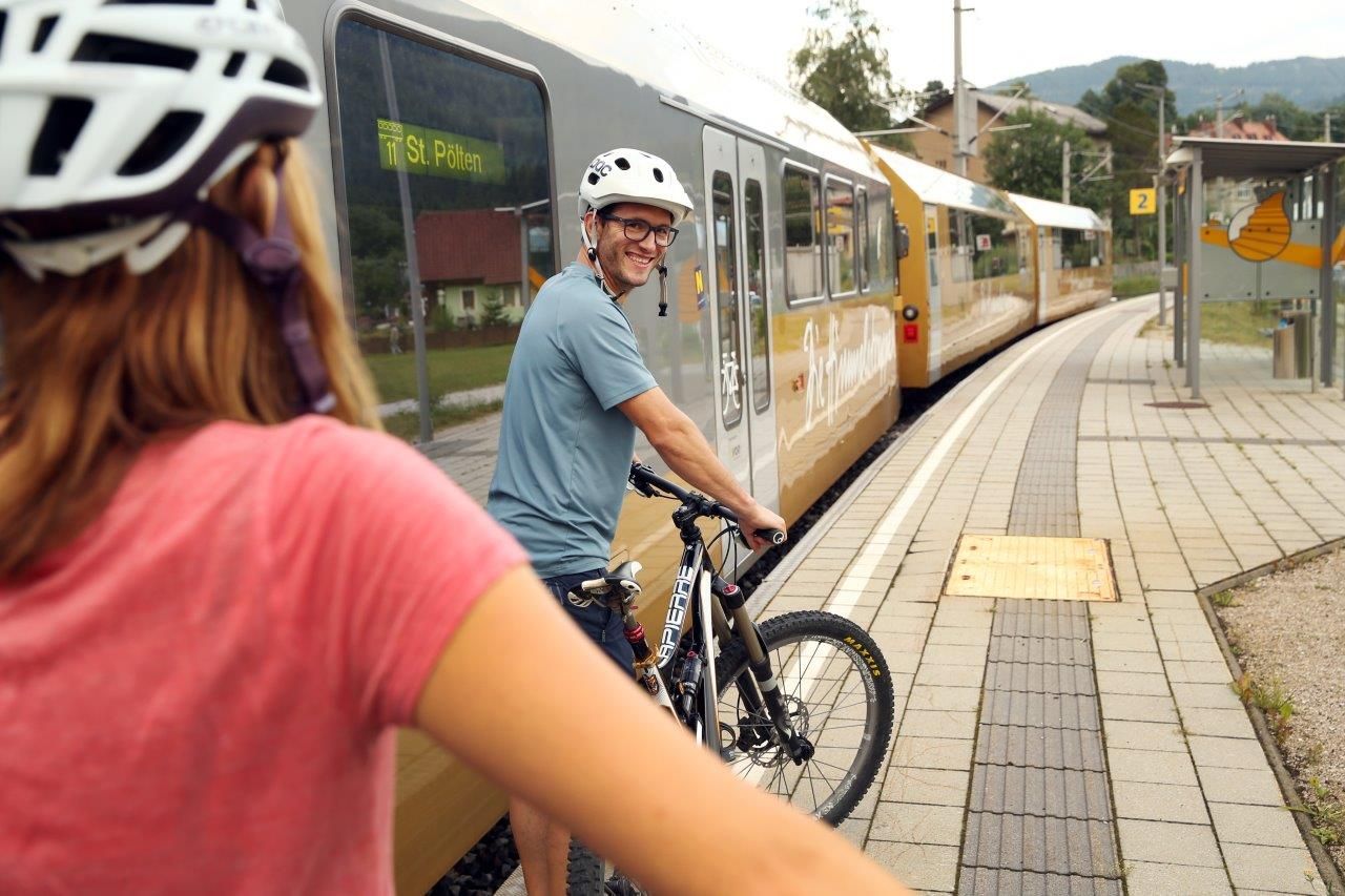 Two people with bicycle helmets are pushing their bikes on the platform, with the stairway to heaven on the tracks next to them.