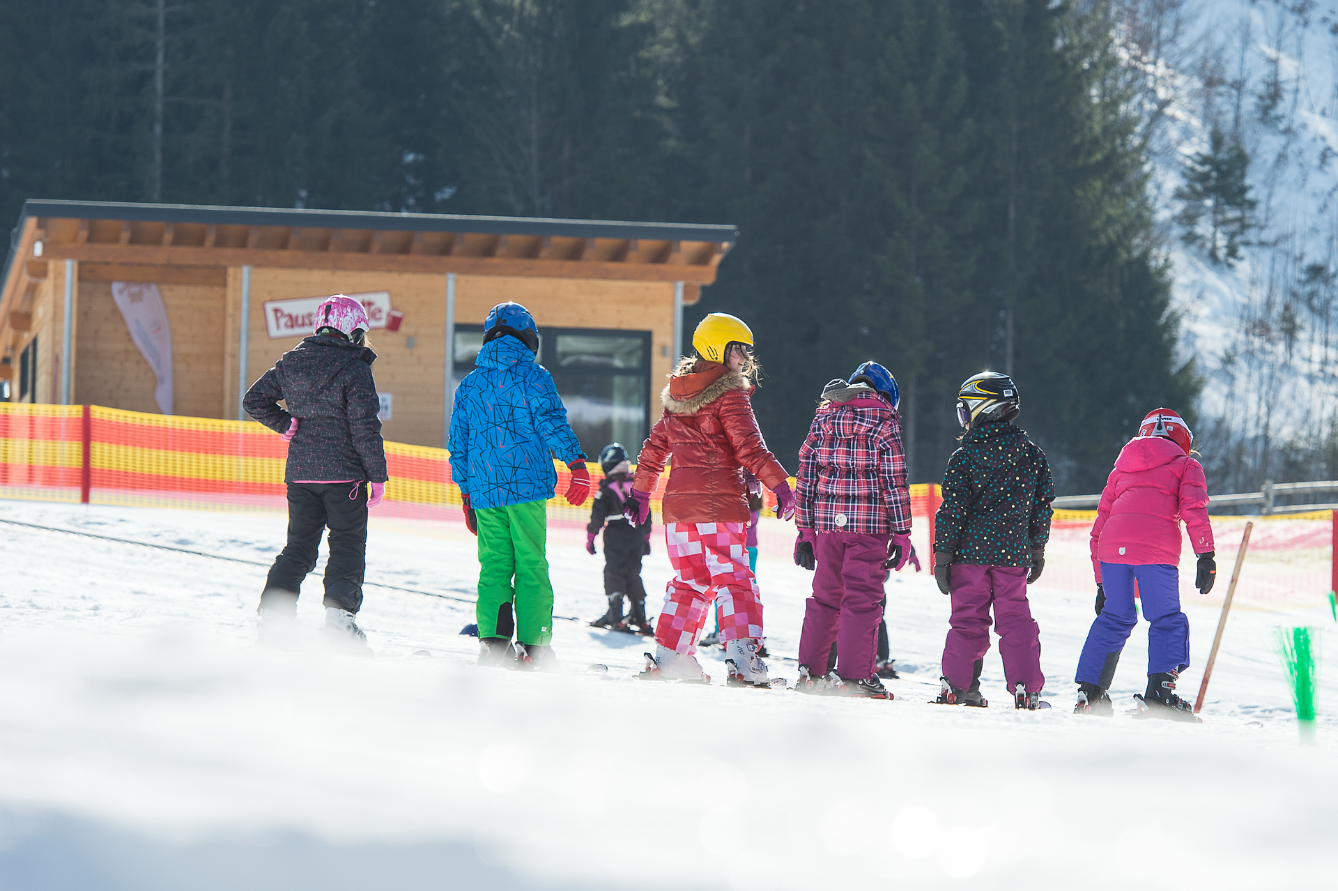 Eine Gruppe fröhlicher Kinder in bunten Skianzügen gleitet über die schneebedeckten Hänge, während die Sonne strahlend am Himmel steht. Die frische Bergluft und das Lachen der Kleinen schaffen eine unvergessliche Winteratmosphäre, die zum Skifahren und Spielen einlädt.