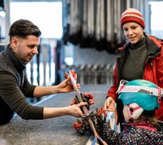 Eine Familie will sich Ski für ihre Tochter ausborgen. Sie werden von einem kompetenten Mitarbeiter beraten. Alle haben bereits ihre Skikleidung an.
