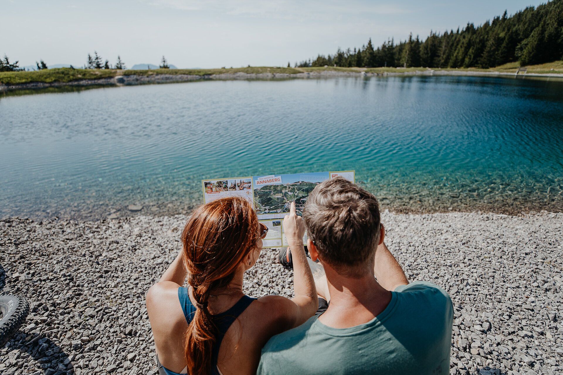 Ein Mann und eine Frau erkunden die Umgebung rund um den Speichersee am Hennesteck am Annaberg mit dem Fahrrad. Sie sind auf den Wegen rund um den See unterwegs und entdecken dabei die alpine Landschaft mit ihren Bergen, Wiesen und Aussichtspunkten.
