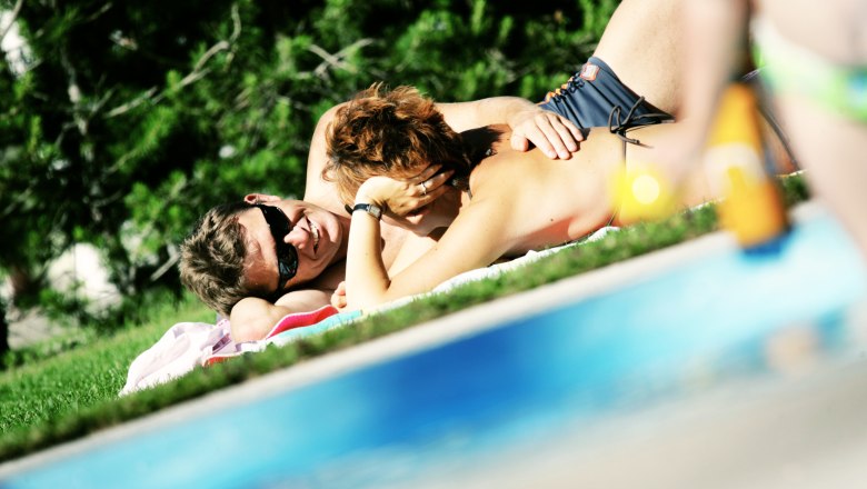A couple is relaxing on a lawn next to a pool.