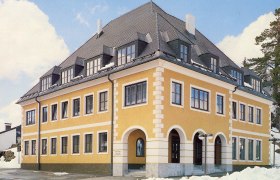 Gelbes Geb&auml;ude mit grauem Dach und vielen Fenstern, umgeben von Schnee.