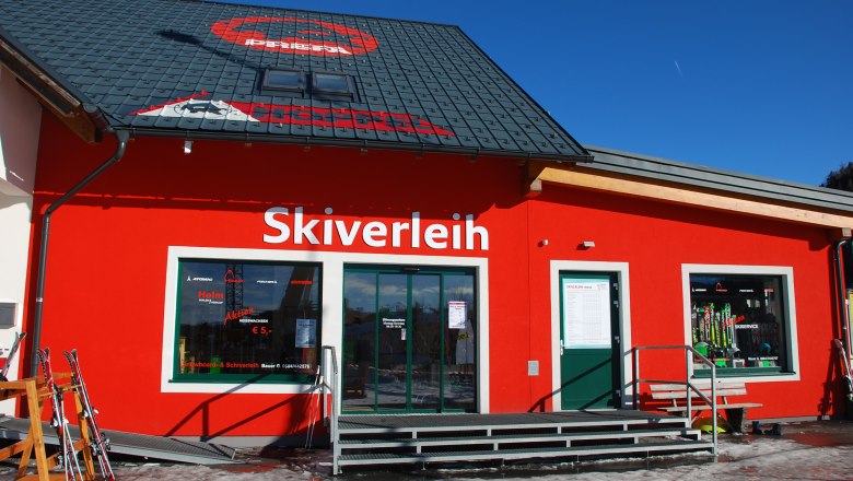 Ein rotes Gebäude mit der Aufschrift 'Skiverleih' und Skiausrüstung im Schaufenster.