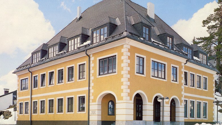 Gelbes Geb&auml;ude mit grauem Dach und vielen Fenstern, umgeben von Schnee.