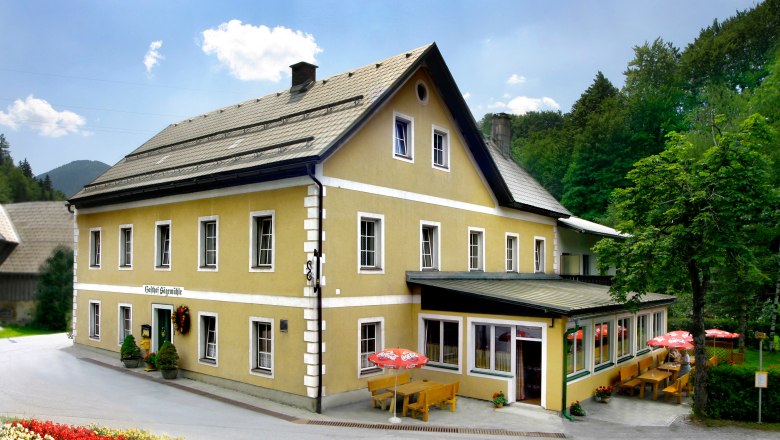 Gasthof Sägemühle, © zVg Ein gelbes Gasthaus mit Terrasse und Sonnenschirmen, umgeben von Bäumen.