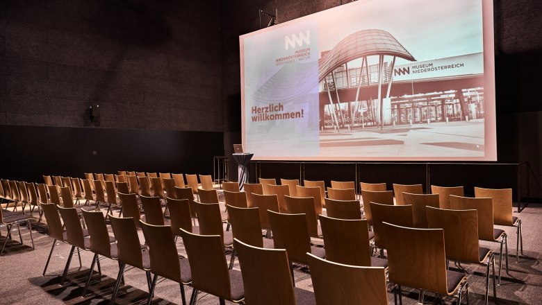 Empty cinema hall in the Museum Niederösterreich with rows of chairs and a large screen.