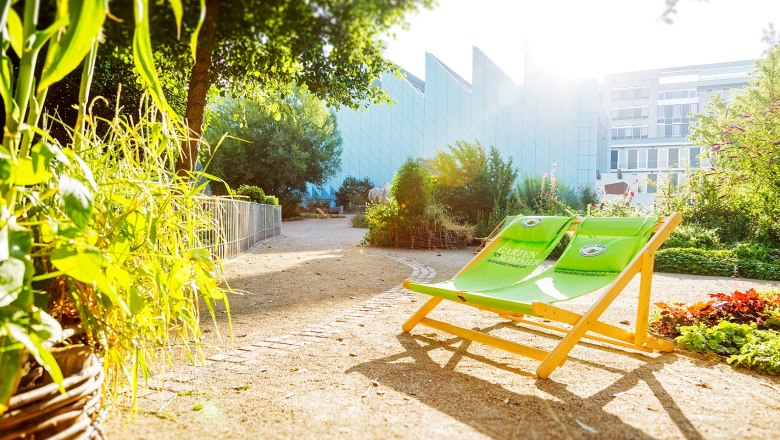 Garden area of the Museum Niederösterreich with green deckchairs and plants in the sunlight.