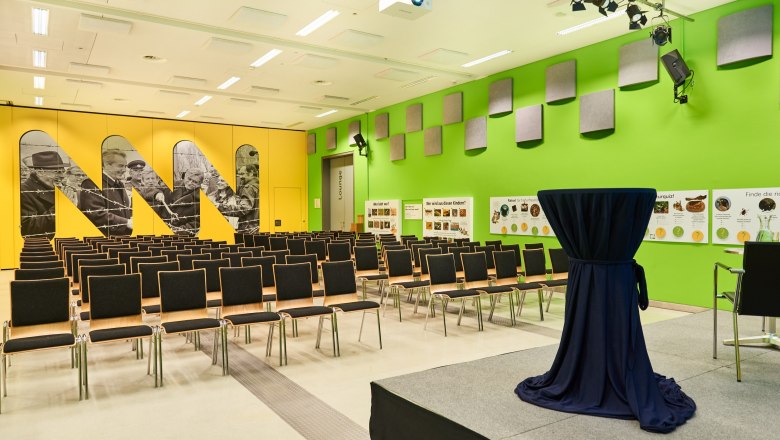 A conference room in the Museum Niederösterreich with a yellow and green wall, rows of chairs and a high table on a stage.