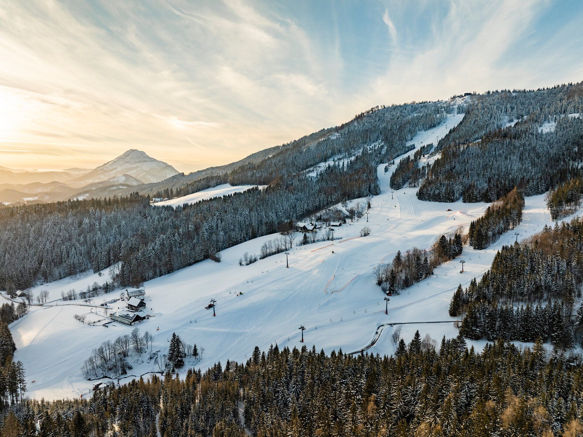 Aus der Vogelperspektive eröffnet sich ein weiter Blick über das Skigebiet Annaberg. Sanfte, schneebedeckte Hänge ziehen sich durch die Landschaft und werden von dunklen Waldstreifen unterbrochen. Die Szene wirkt weitläufig und ruhig und vermittelt ein Gefühl von frischer Winterluft und unberührter Natur.