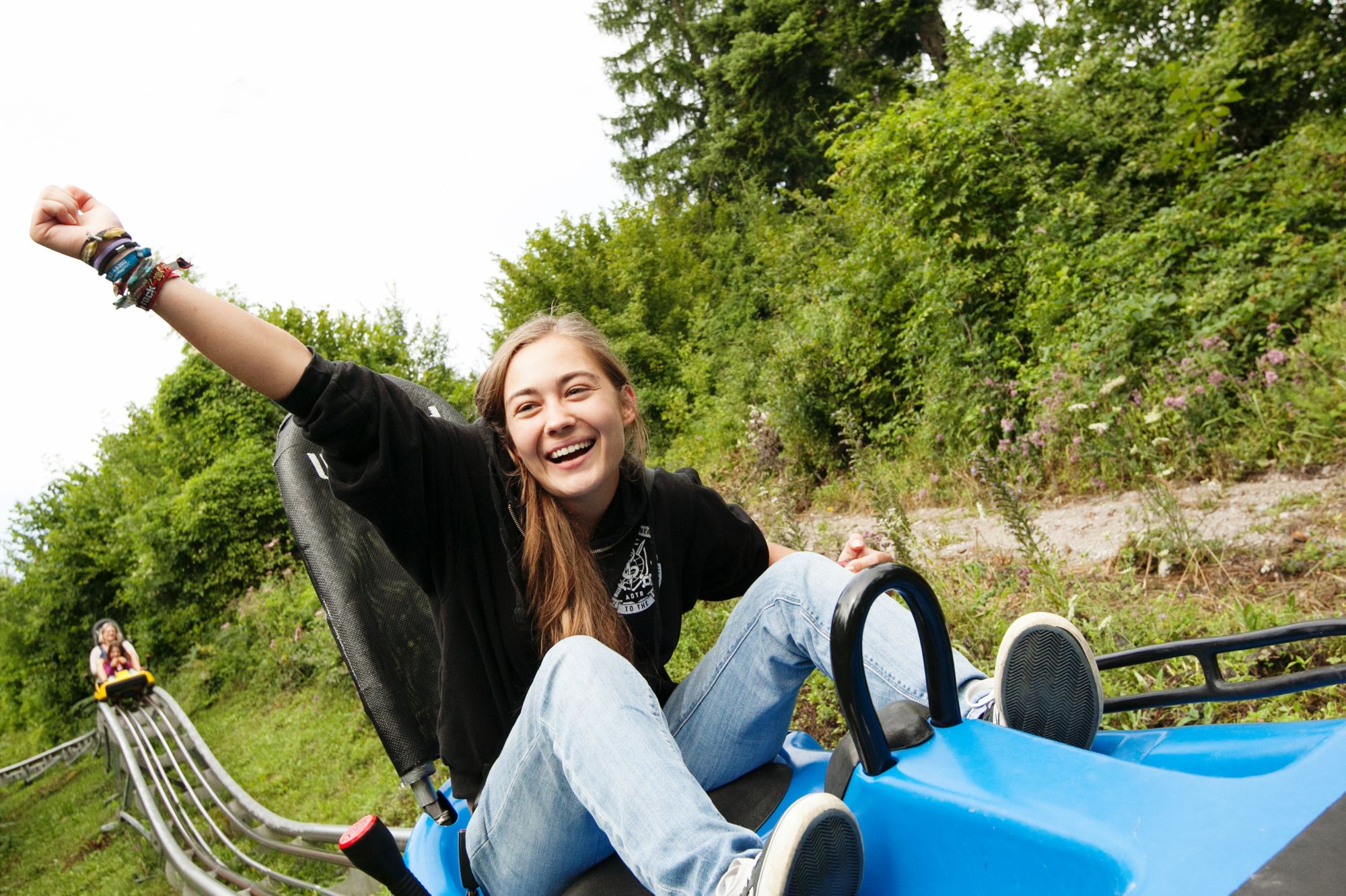 Eine lachende Person fährt auf einer Sommerrodelbahn, umgeben von grüner Natur.