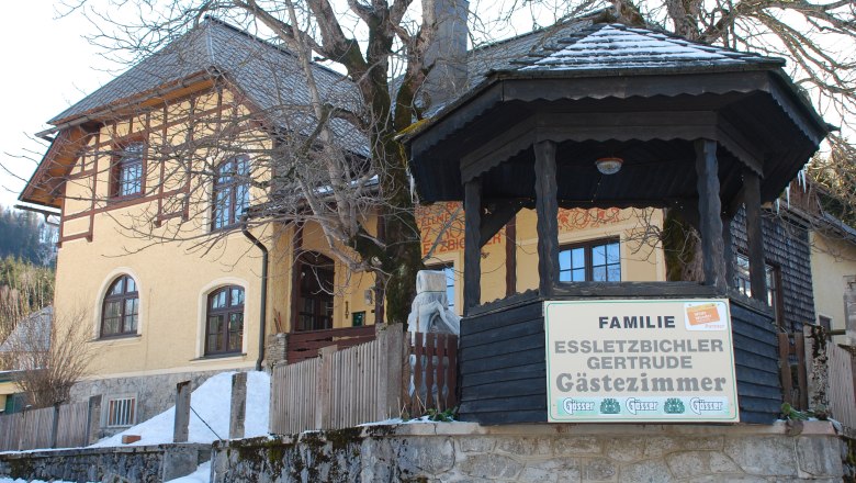 Yellow guest house with wooden veranda and sign 'Familie Essletzbichler Gertrude Gästezimmer'.