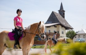 Two female riders on horses in front of a building with a tower.
