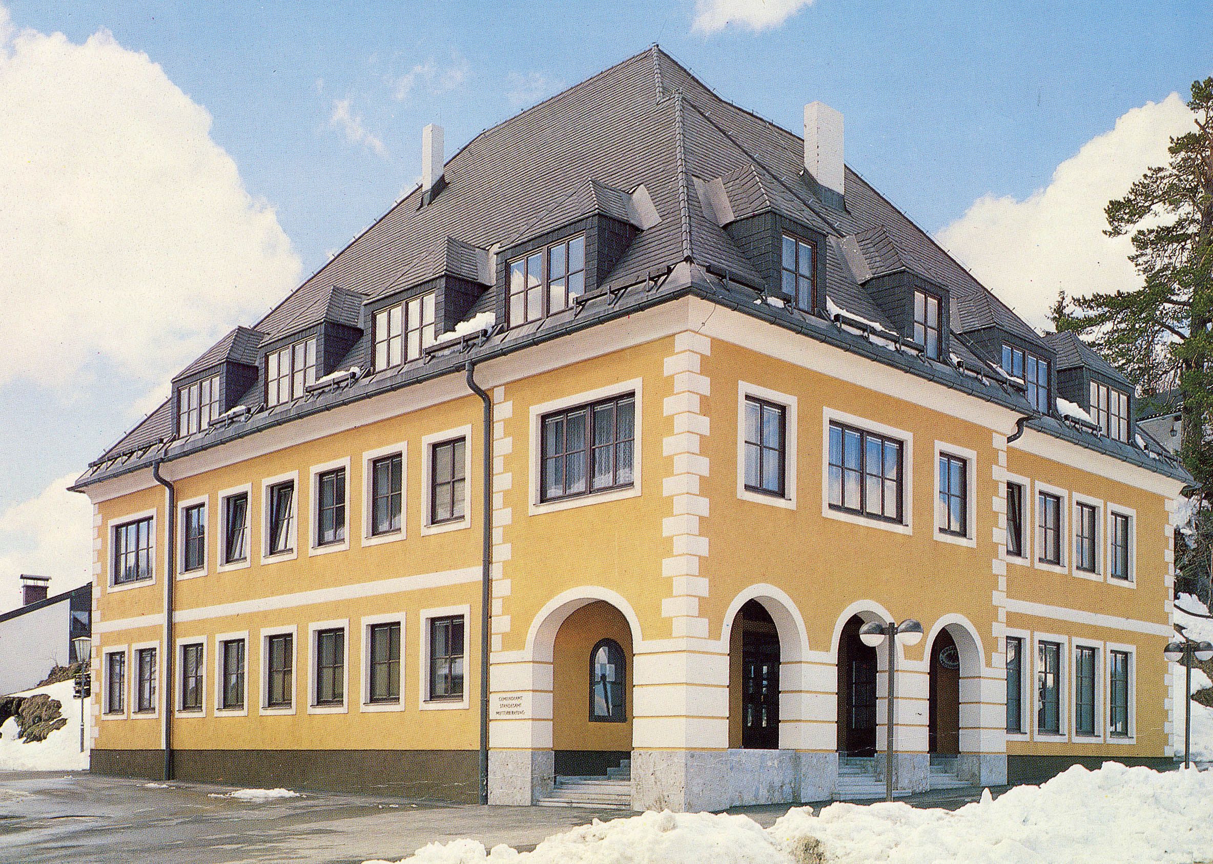 Yellow building with a gray roof and many windows, surrounded by snow.