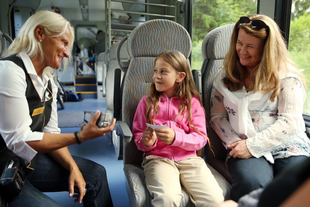 A girl smilingly hands her ticket to the conductor on the train.
