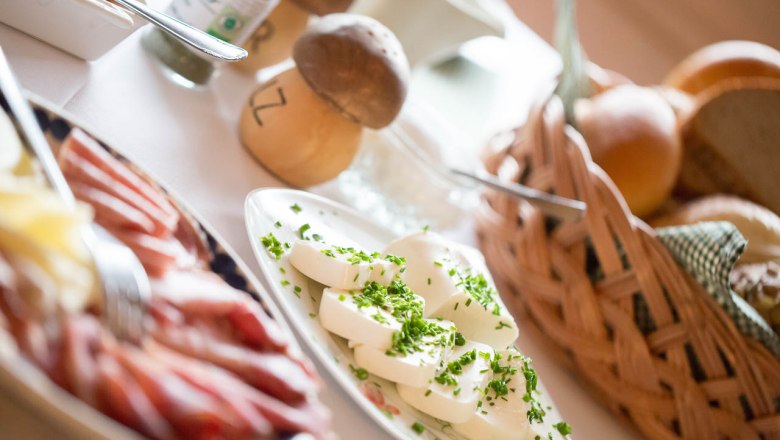 Ein Frühstückstisch mit Käse, Schinken, Brötchen und Kräutern.