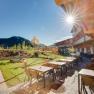 Terrasse des JUFA Hotels Annaberg mit Tischen, Stühlen und Spielplatz im Hintergrund bei Sonnenschein.