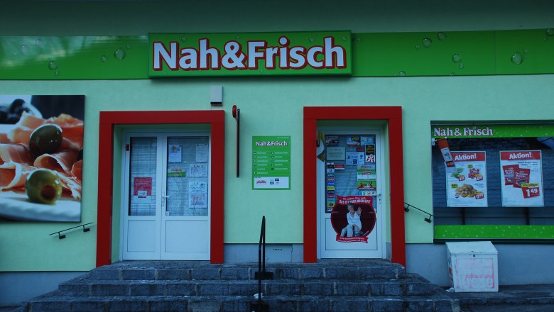 Eingang eines Nah&Frisch-Ladens mit Werbeplakaten und Schaufenster.