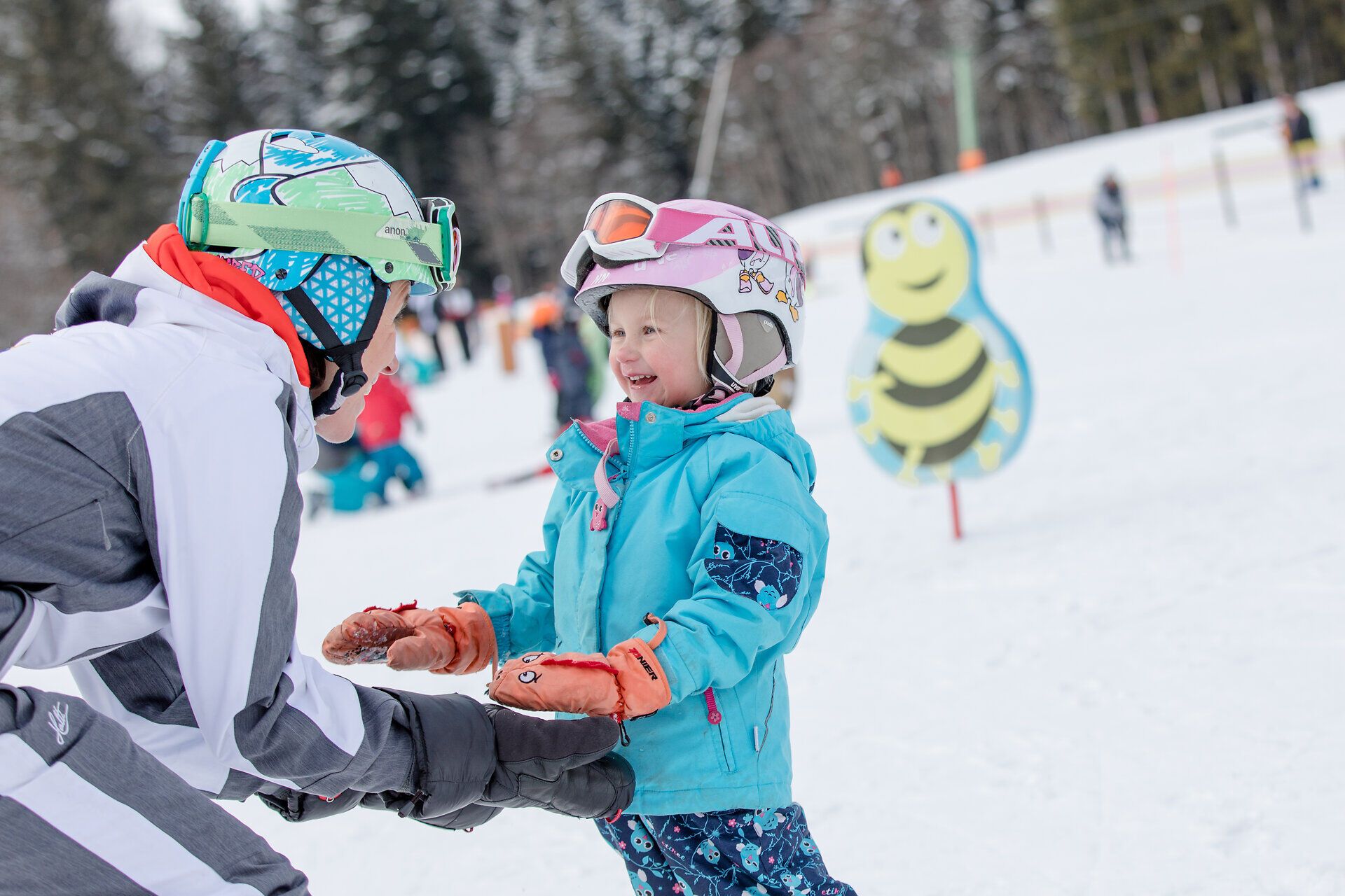 Ein fröhliches Kind genießt den Wintertag auf den Pisten von Annaberg, während es mit einem Skilehrer interagiert. Die schneebedeckten Berge und die frische, klare Luft schaffen eine perfekte Kulisse für unvergessliche Familienmomente.