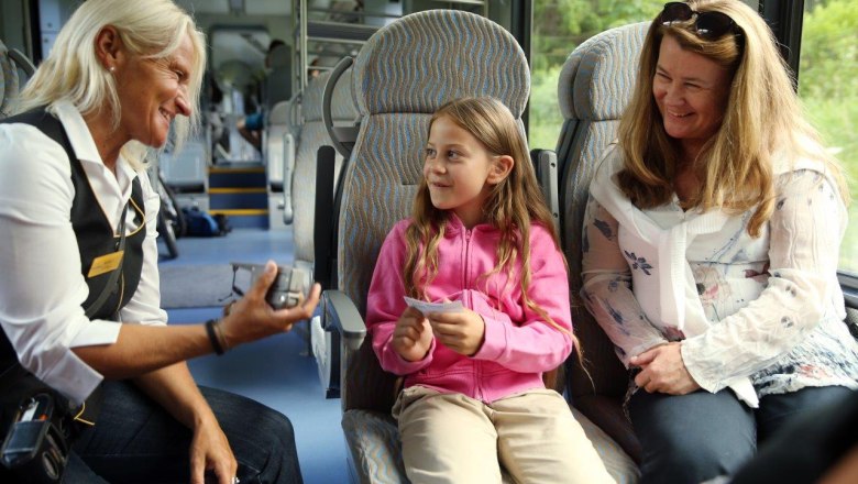 Ein Mädchen reicht der Schaffnerin in der Bahn lächelnd ihr Ticket.