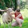 A woman and two children are stroking a sheep in a meadow.